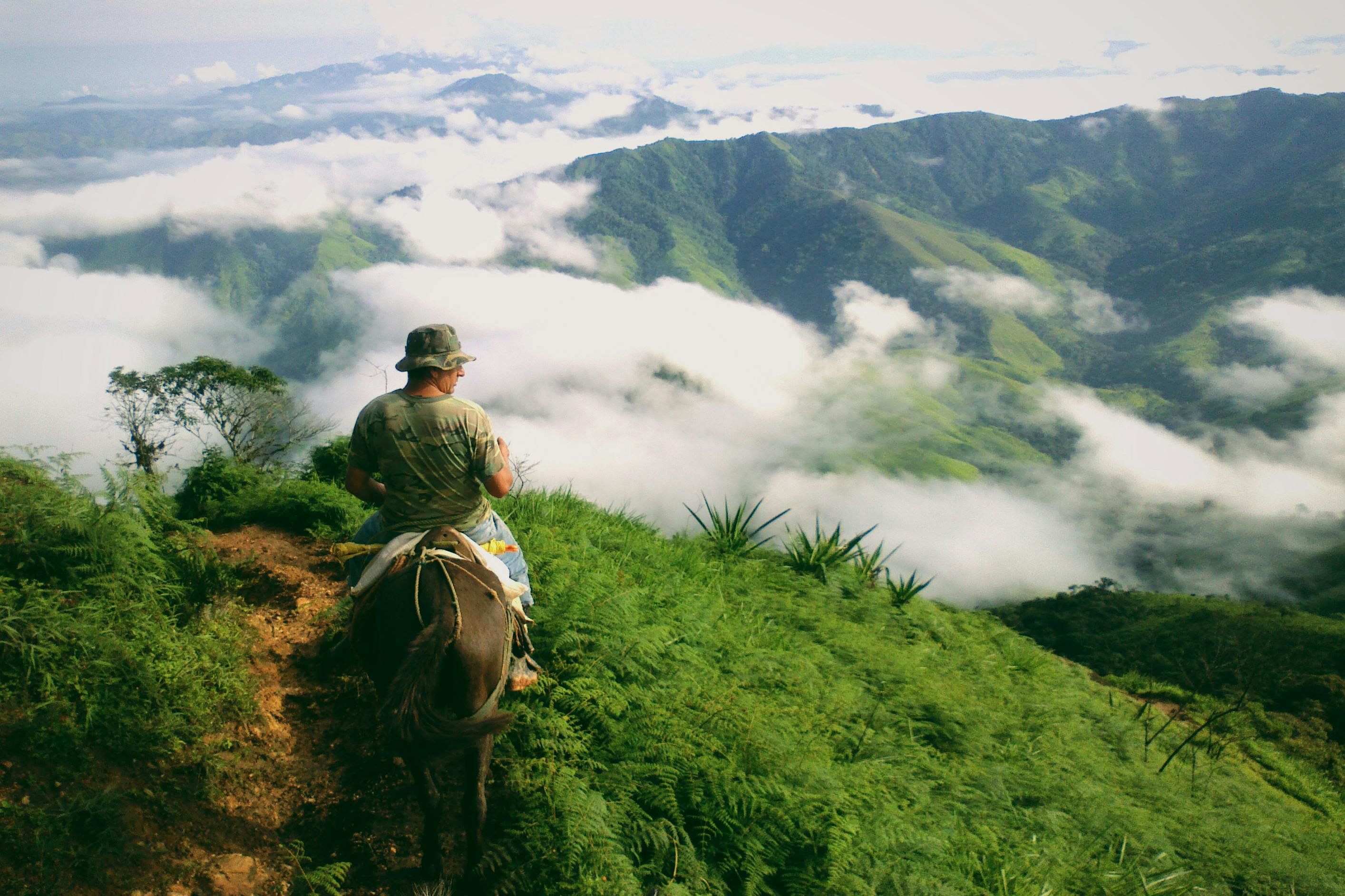 a person riding a horse with green cloudy mountains in the backdrop