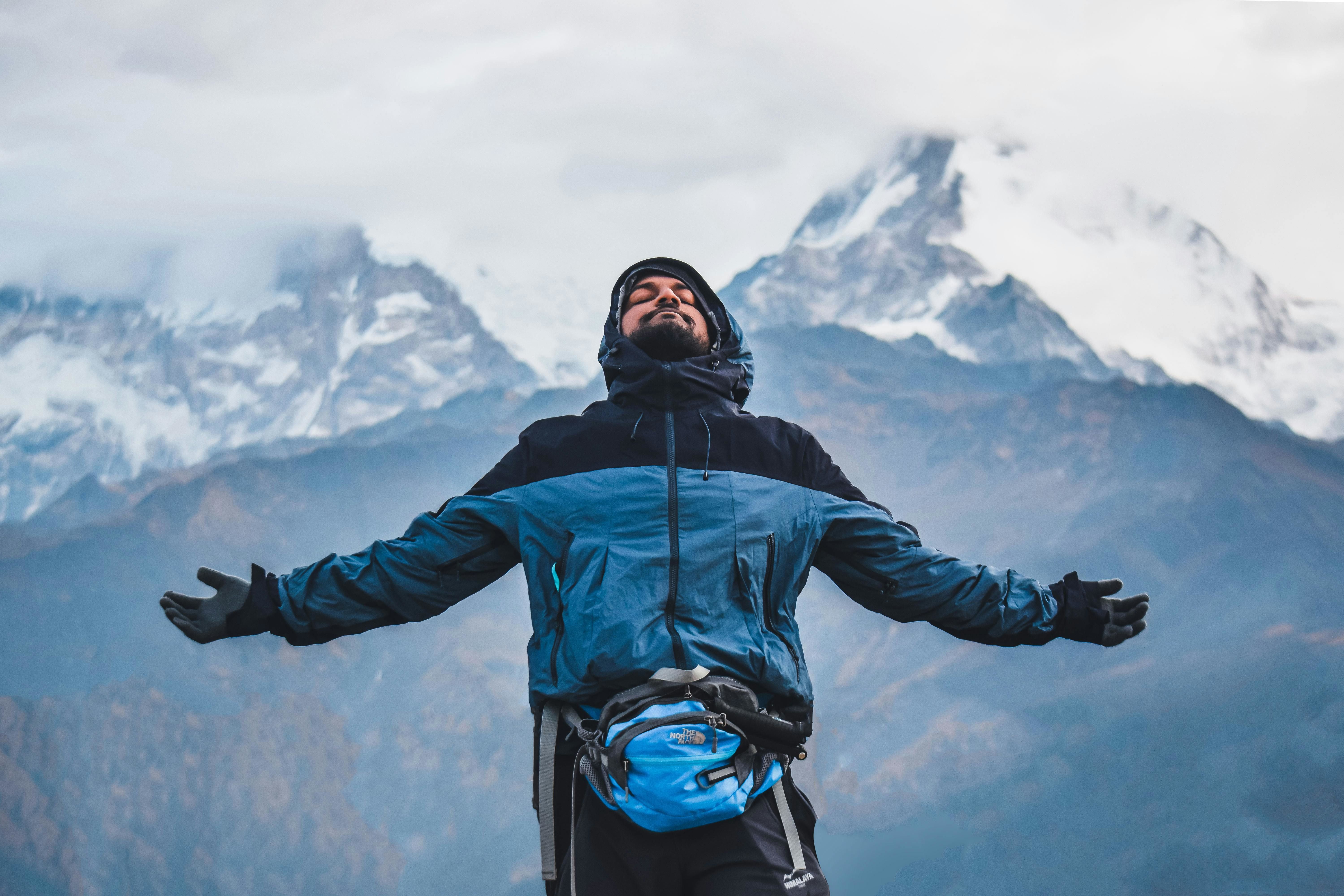 a person standing with open arms with snow capped mountains in the backdrop