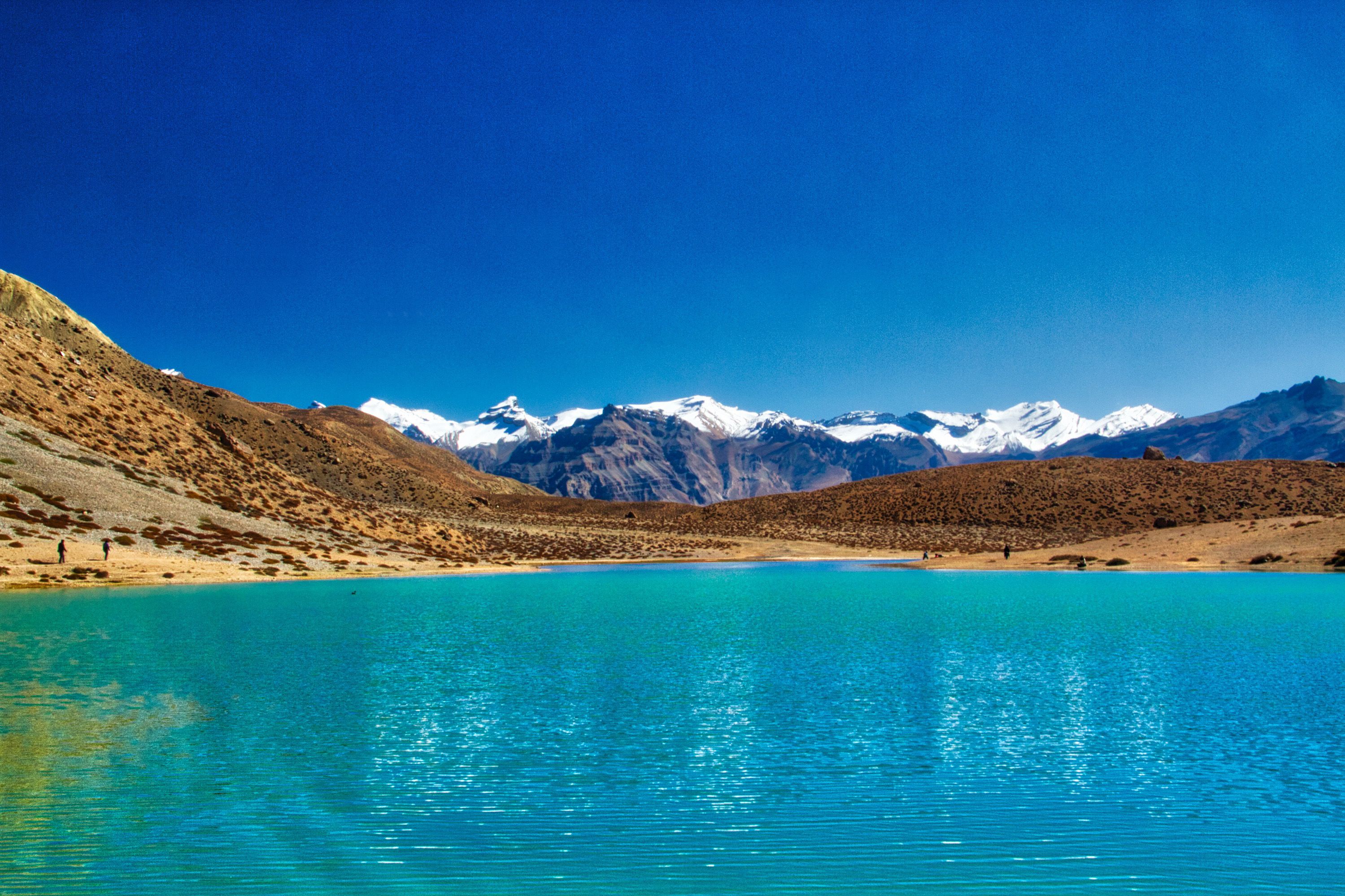 blue coloured water in dhankar lake with snow capped mountain in the backdrop during daytime