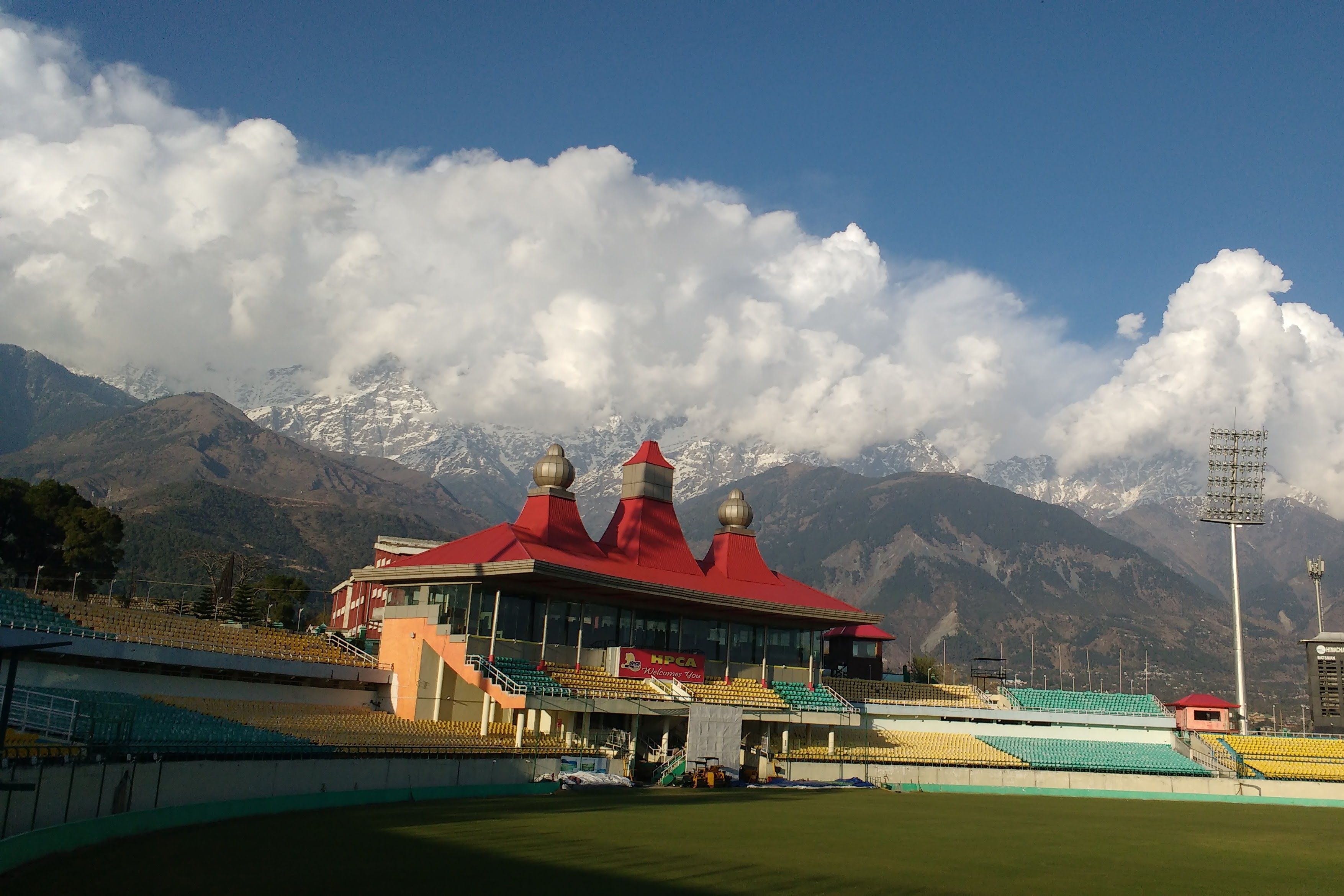 cricket stadium in dharamshala with  brown mountains in the backdrop covered in clouds