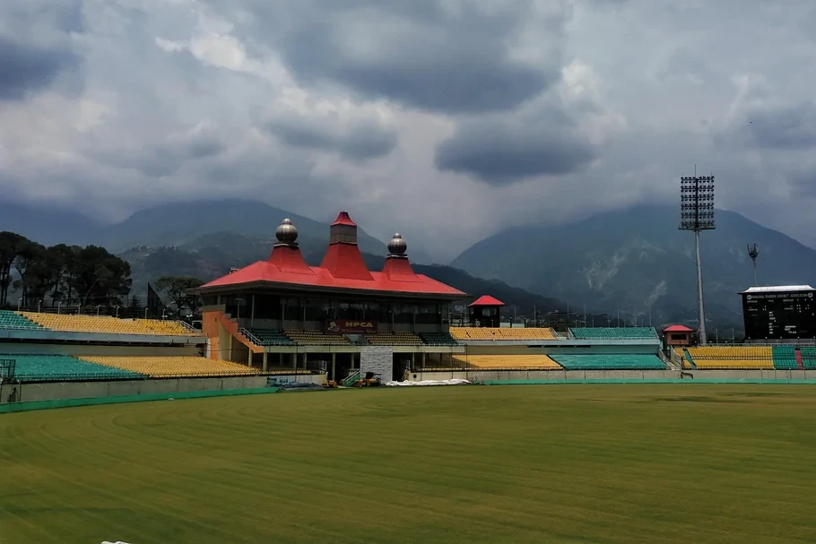 cricket stadium in dharamshala with  brown mountains in the backdrop on a cloudy day