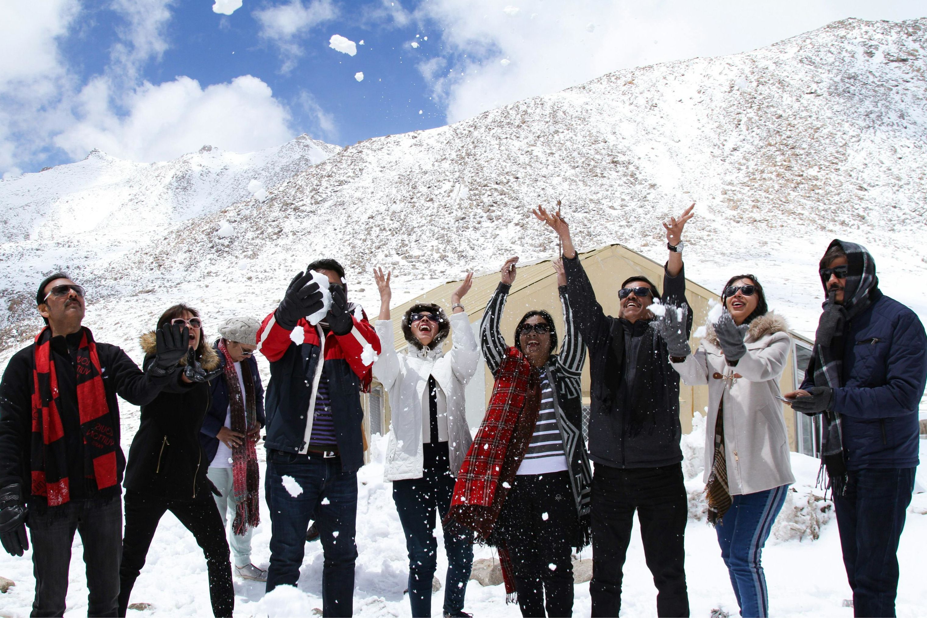 a group of people standing in a mountain valley and throwing snow in the air and smiling