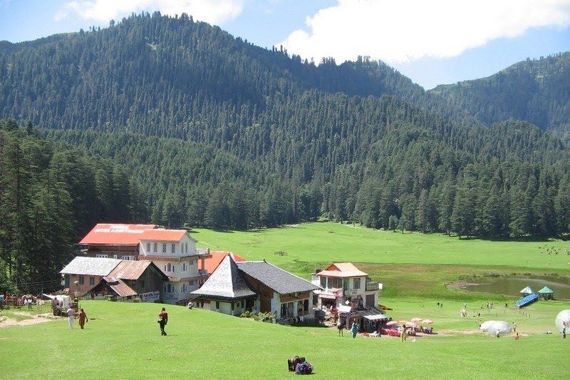 houses in the field near a small lake surrounded by mountains in khajjiar