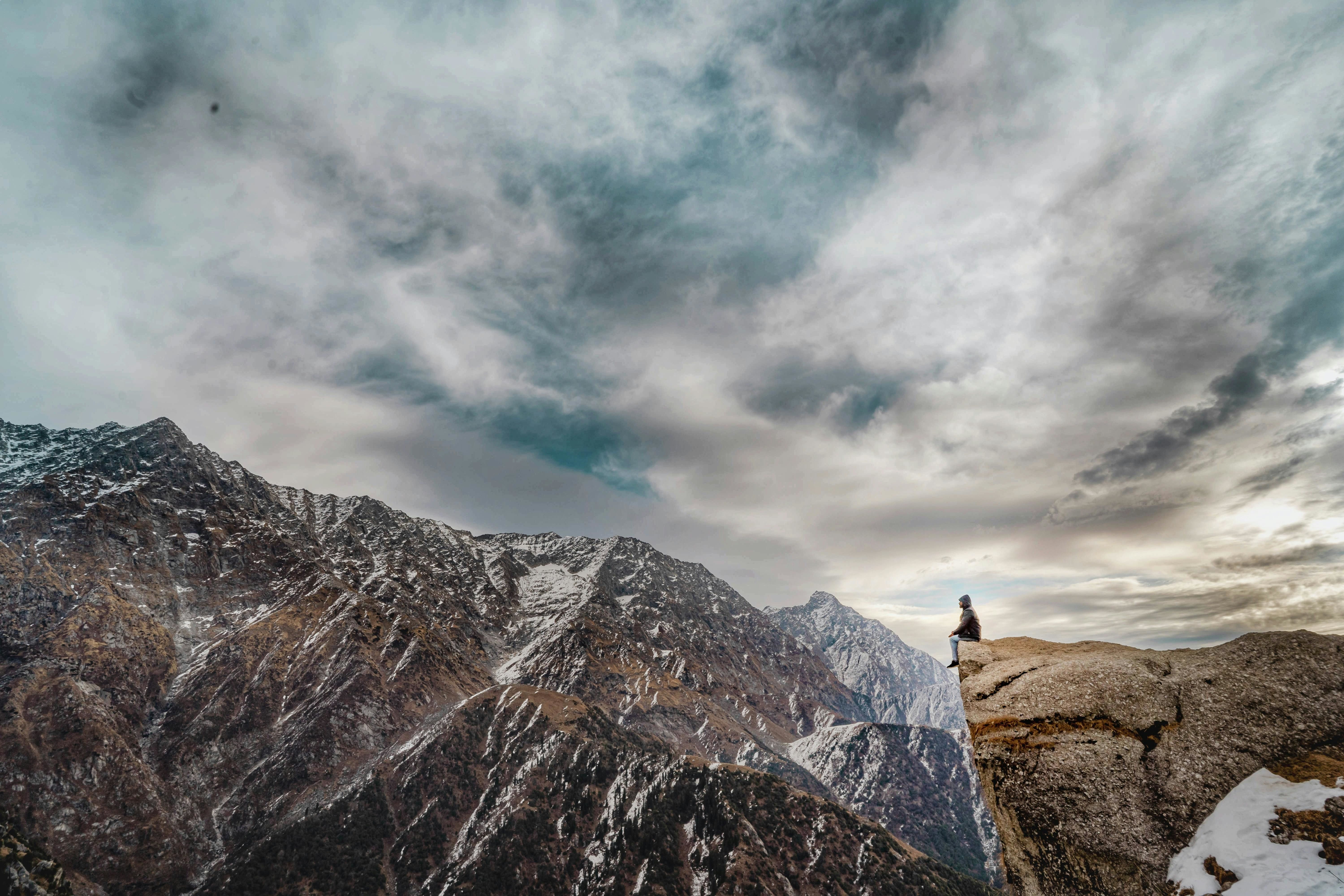a person sitting on a rock with snow covered mountain in the backdrop