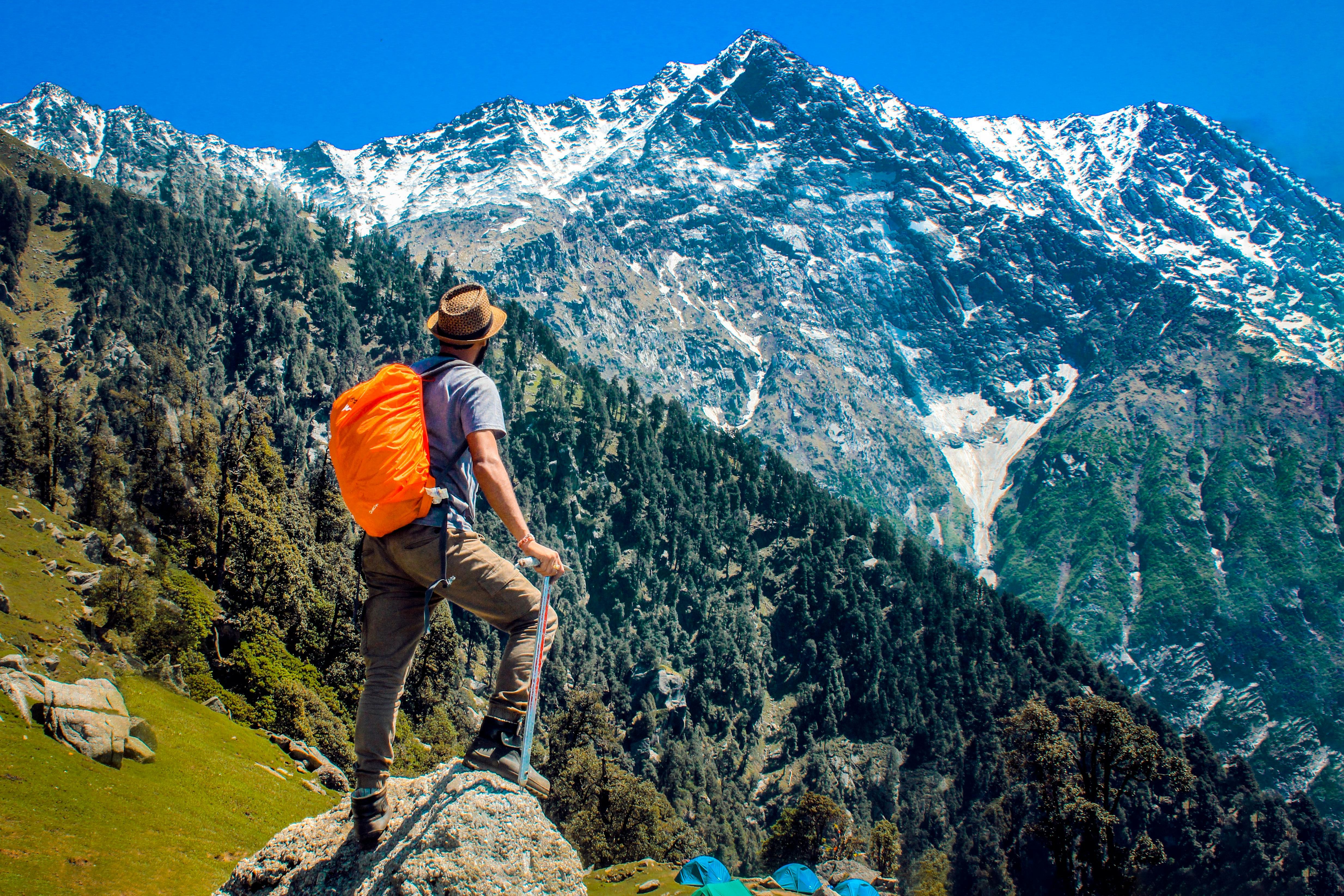 man wearing blue shirt standing on cliff while watching mountain