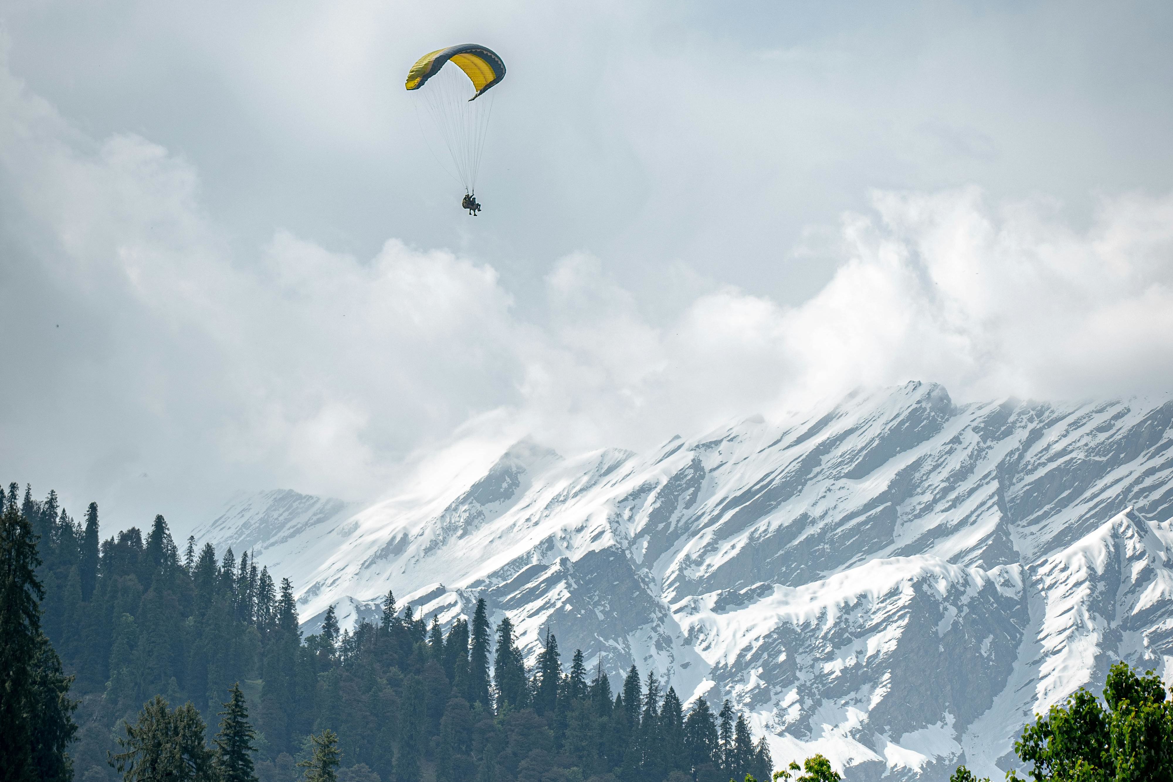 a person paragliding near solang valley with snow covered mountains in the backdrop