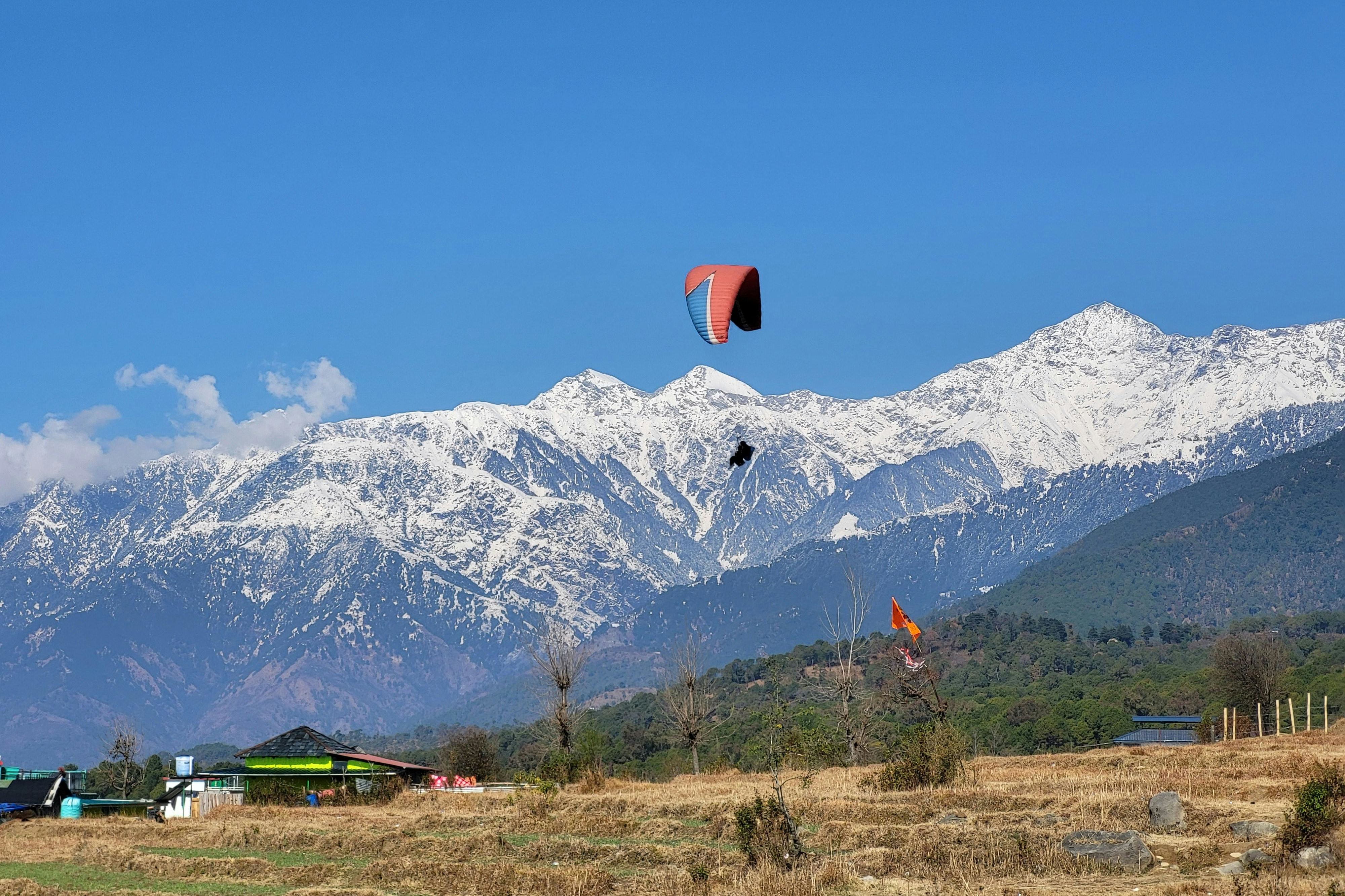 a person paragliding in bir village with snow covered mounatin in the backdrop